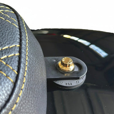 Close-up of Bamco ARP stainless steel gold-plated 12-point seat bolt securing a Harley-Davidson seat bracket beside black leather seat with yellow contrast stitching