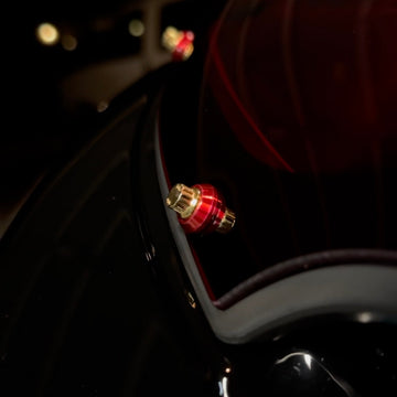 Close-up of Bamco red anodized cap covering ARP stainless steel bolt on black Harley-Davidson motorcycle near taillight