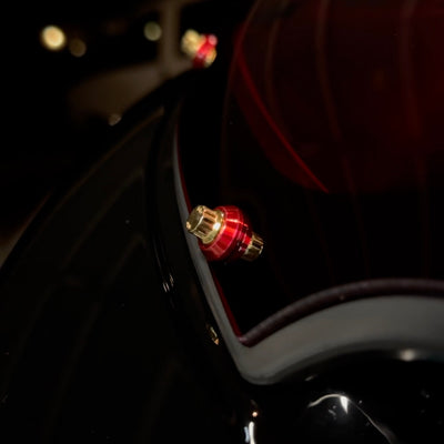 Close-up of Bamco red anodized cap covering ARP stainless steel bolt on black Harley-Davidson motorcycle near taillight