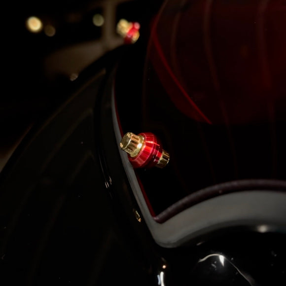 Close-up of Bamco red anodized cap covering ARP stainless steel bolt on black Harley-Davidson motorcycle near taillight