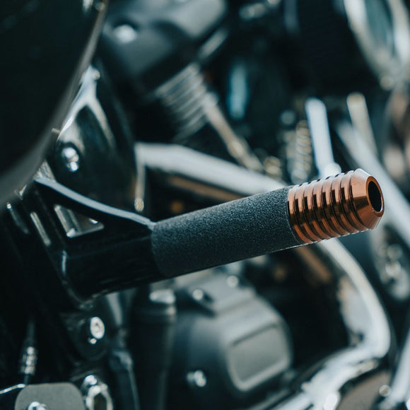 Motorcycle foot peg with black foam grip and copper ribbed end cap