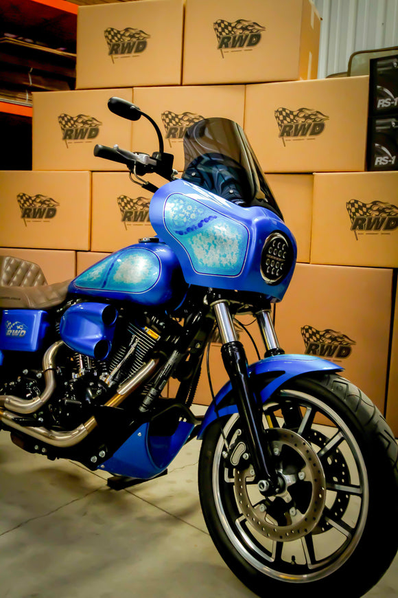 A custom blue RWD V-Twin motorcycle with a fairing, LED headlight, and custom paintwork, parked in front of stacked RWD branded boxes.