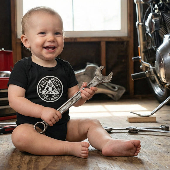 Baby in a speed kings onesie holding a wrench