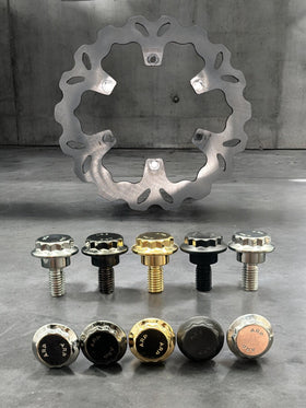 ARP stainless steel Harley-Davidson rotor bolts by Bamco in chrome, black and gold finishes arranged in front of a motorcycle brake rotor