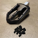 Black flat bicycle pedal with pile of black set screws (replacement pins) on concrete surface