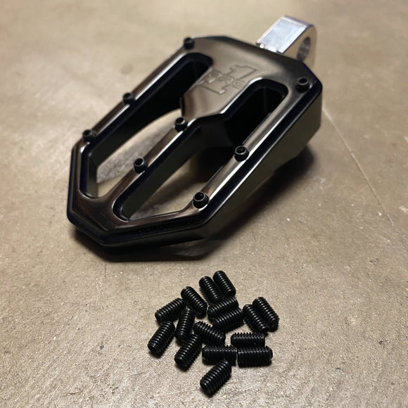 Black flat bicycle pedal with pile of black set screws (replacement pins) on concrete surface